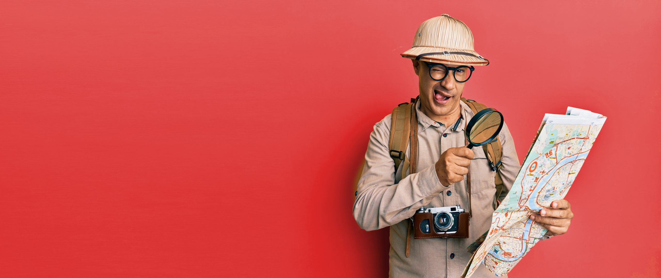 Man wearing a adventurer outfit holding a map against a red background